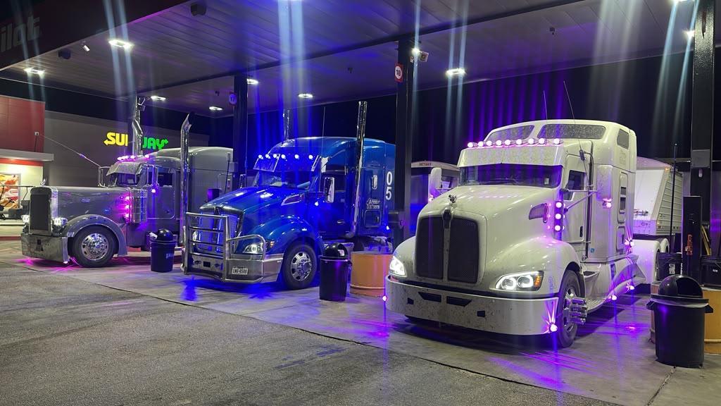 Three AREN Peterbilt and Kenworth trucks fueling at a Texas truck stop at night